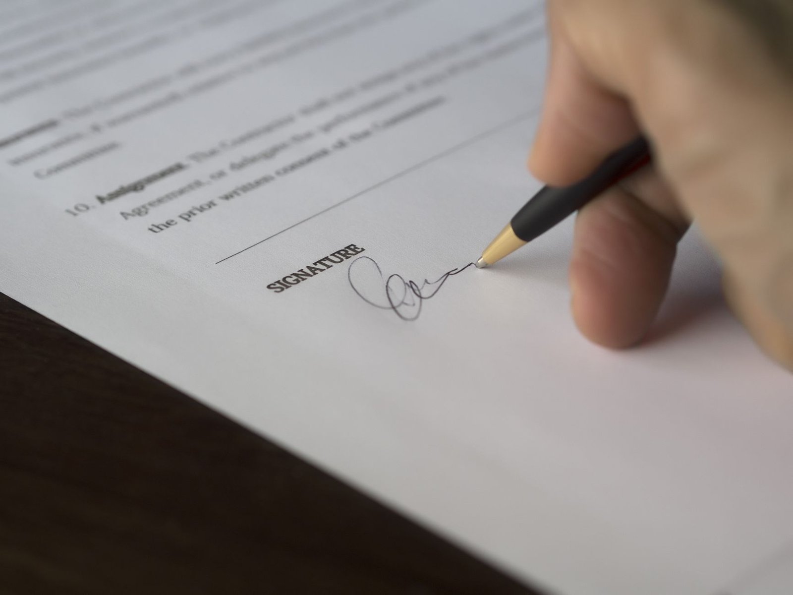 A hand signing a formal document on a wooden desk